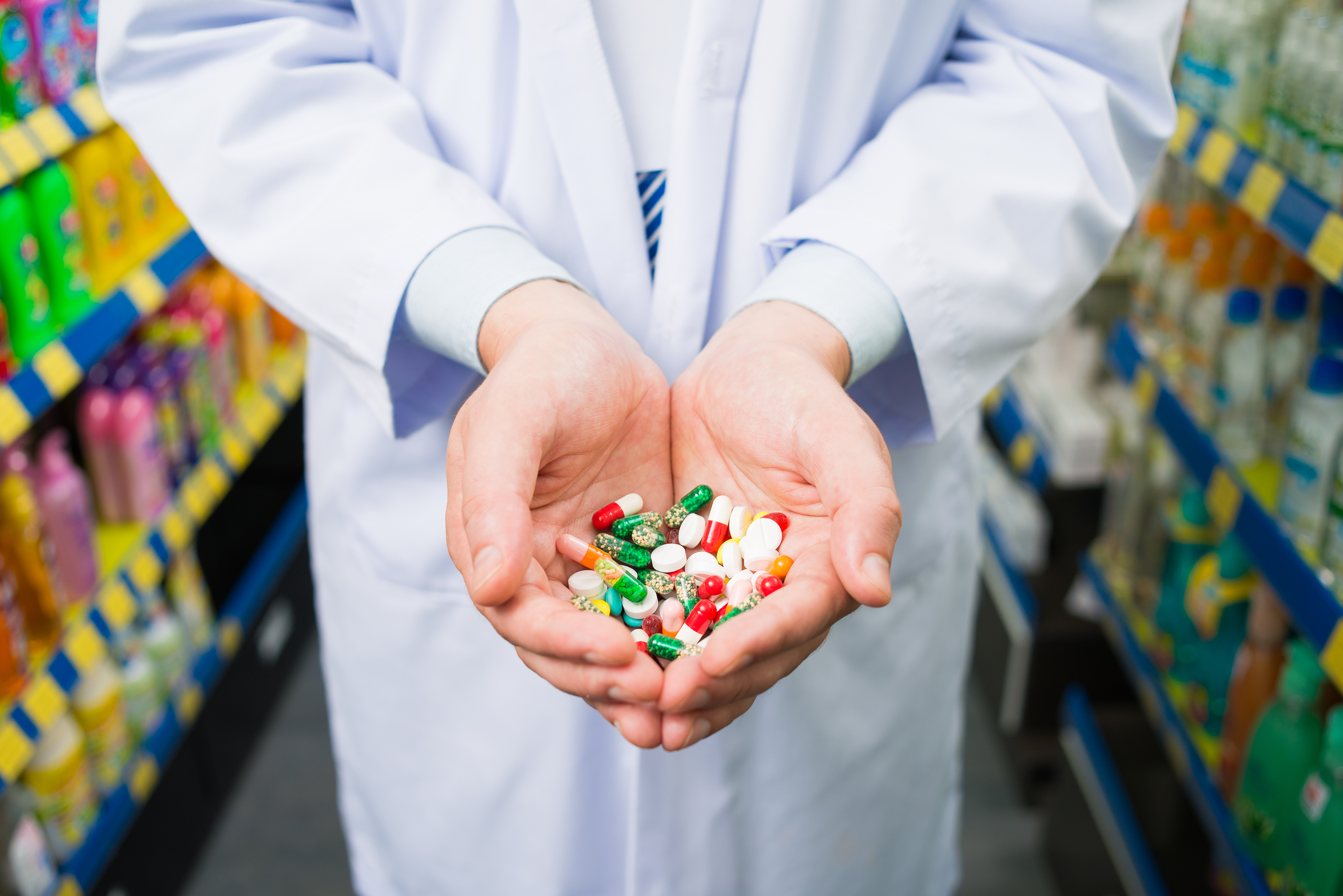 Cropped image of a pharmacist holding many colorful pills in the palms on the foreground