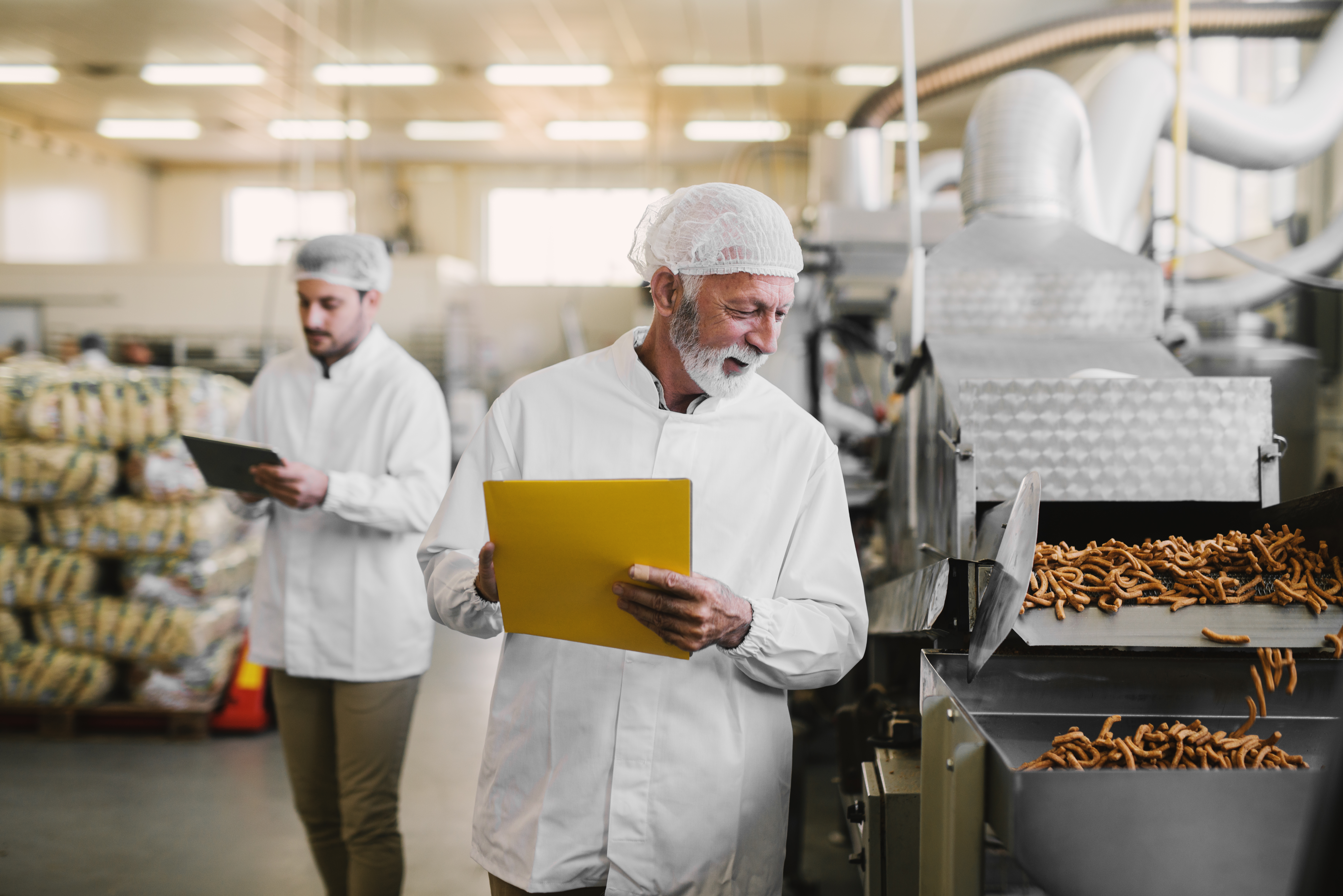 Father and son walking through their food factory in sterile clothes . Taking notes about food quality and looking satisfied.